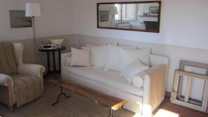 Ein Wohnzimmer mit einem weißen Sofa, einer Holzbank, einer Stehlampe und einem Spiegel an der Wand.