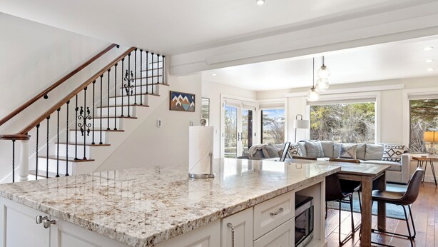 A spacious kitchen with a granite countertop, white cabinetry, and a wooden staircase. - Outpost: Teton Shadows South Teton F (Jackson)