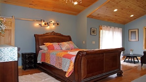 Quarto com cama de madeira, mesa de cabeceira, cômoda e uma pequena mesa redonda com um vaso.