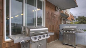 Ein Patio-Bereich mit einem Grill aus Edelstahl und einer kleineren Kochstation, beide auf Rollen, vor einer Holzwand und einem Fenster.