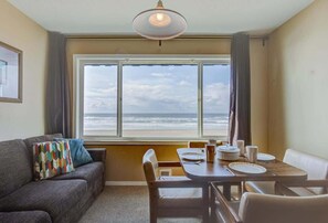 Ein Zimmer mit großem Fenster und Meerblick, einem gedeckten Esstisch sowie einer Couch mit farbigem Kissen.