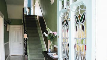 A hallway with a staircase, a decorative door with stained glass, and a hanging light fixture.