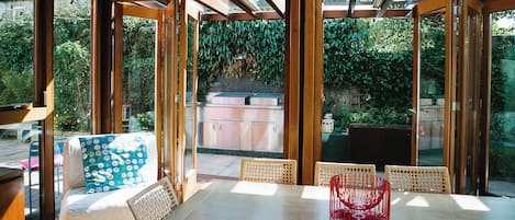 An outdoor entertaining area with a wooden pergola, a dining table with chairs, and a view of a garden.