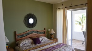 Una camera da letto con un letto, un comodino, una lampada, uno specchio a parete e una porta scorrevole in vetro che dà su un balcone.
