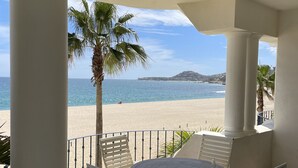 Un balcone con vista sulla spiaggia, colonne bianche e un tavolo rotondo con sedie.