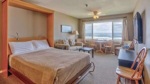 Une chambre d’hôtel avec un lit, un bureau, une chaise, une petite table et une vue sur l’océan.
