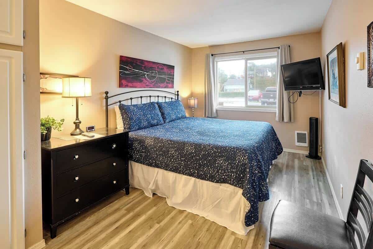 A bedroom with a bed, a dresser, a TV, and a window with a view of the outside.