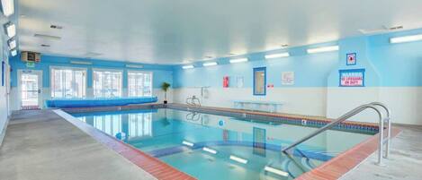 Una piscina interior con agua cristalina, un borde de ladrillo rojo y una pared azul y blanca.