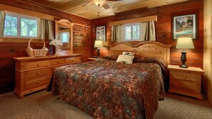 A wooden cabin bedroom with a bed, dresser, nightstand, and ceiling fan.