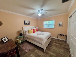 Une chambre à coucher avec un lit, un ventilateur de plafond, une fenêtre avec des stores et une porte.