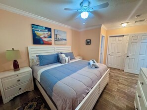 Ein Schlafzimmer mit einem Bett, Nachttischen, einer Lampe, einem Deckenventilator und Kunstwerken an den Wänden.