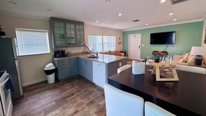 A modern kitchen with a central island, a dining area with a table and chairs, and a living room with a sofa and a flat-screen TV. - 2-Bedroom Apartment Just A Short Walk To Deerfield Beach Pier (Deerfield Beach)