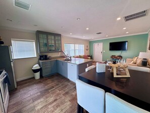 Een moderne keuken met een centraal eiland, een eetgedeelte met een tafel en stoelen, en een woonkamer met een bank en een flatscreen-televisie.