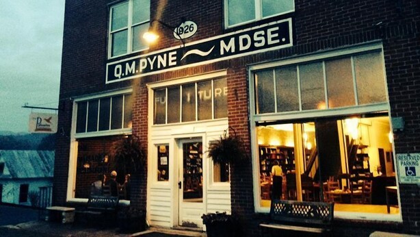 Un bâtiment à deux étages, sur lequel on peut lire l’inscription « Q.M.PYNE MDSE. », et qui possède une grande vitrine au rez-de-chaussée.