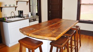 Une cuisine avec une table et des tabourets en bois, un évier et des étagères remplies de tasses et de verres.