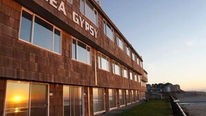 Ein mehrstöckiges Gebäude mit dem Schriftzug "SEA GYPSY" auf der Fassade, großen Fenstern und Blick auf den Strand.