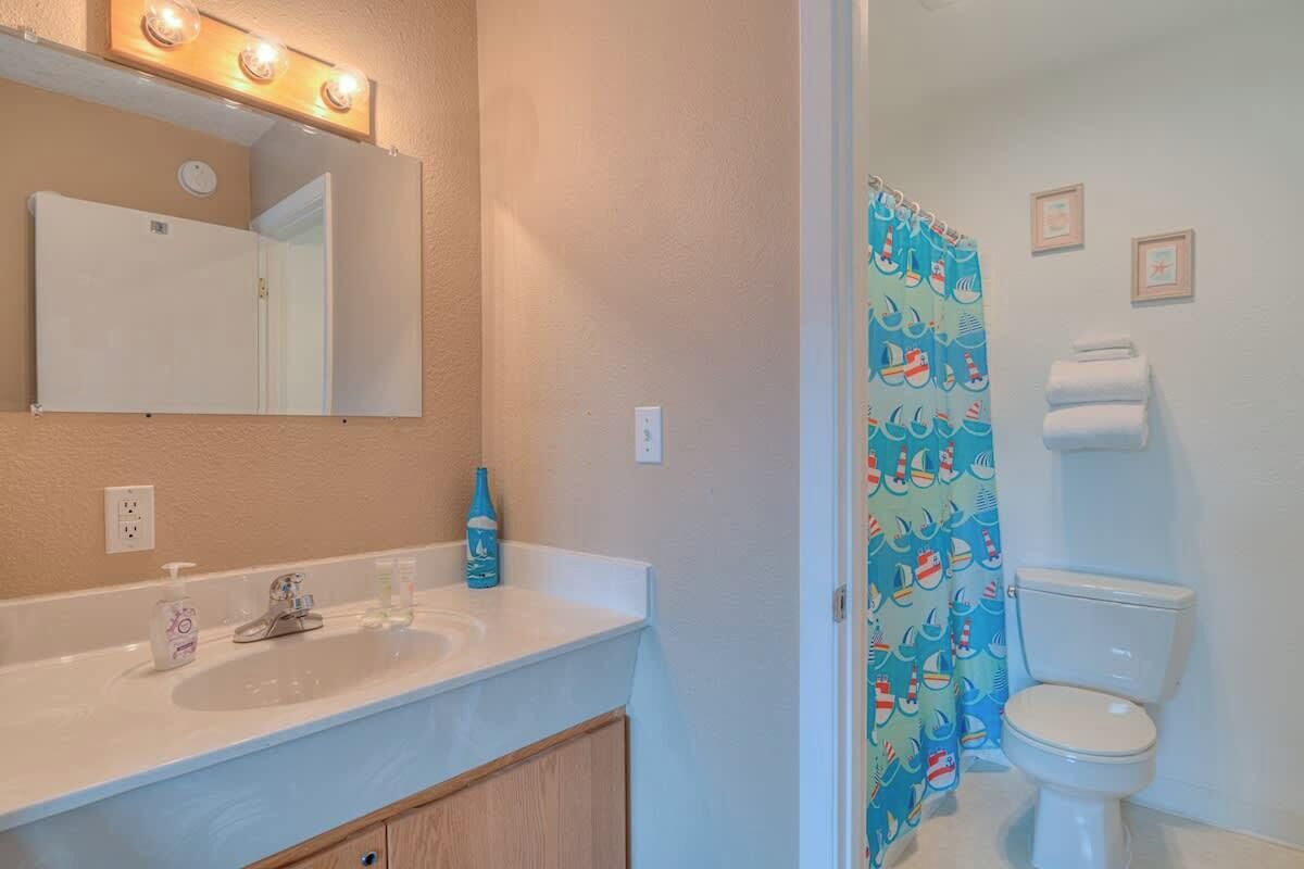 A bathroom with a white sink, mirror, and toilet. There is a shower curtain with a nautical theme.
