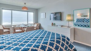 Ein Hotelzimmer mit einem großen Bett, einem Essbereich mit Tisch und Stühlen, einem Fernseher und einem großen Fenster mit Blick.