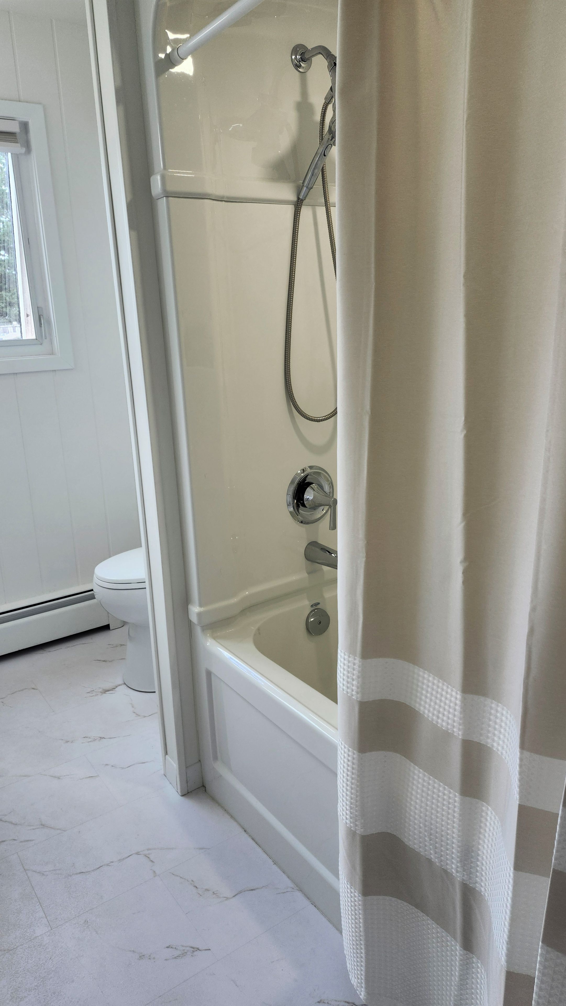 Et badeværelse med en glasafskærmet brusekabine, et hvidt toilet og en gulv med marmorlook.