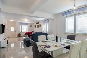 A dining area with a white table set for four, a blue sofa in the background, and a TV on the left. - Resort Villa San Lilin (Nerežišće)