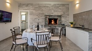 A dining area with a stone fireplace, white cabinets, and a TV on the wall. - Resort Villa San Lilin (Nerežišće)