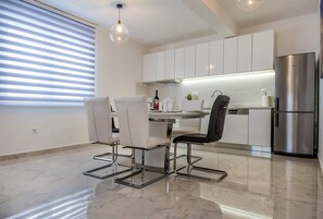 A modern kitchen with white cabinets, a stainless steel refrigerator, and a dining area with a white table and chairs. - Resort Villa San Lilin (Nerežišće)