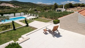 A pool area with a clear view of the surrounding landscape, a covered patio with seating, and a small building with a chimney. - Resort Villa San Lilin (Nerežišće)