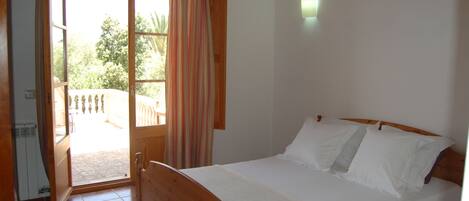 A bedroom with a wooden bed, white bedding, a sliding glass door to a balcony, and a small wall-mounted light.
