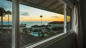 Une vue depuis une fenêtre donnant sur un espace piscine, avec un coucher de soleil en arrière-plan.