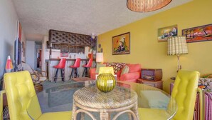 A living room with a glass coffee table, yellow chairs, a red sofa, and a kitchen area in the background. - Retro Oceanfront Suite - Pool and Sauna - Second Floor - Sleeps 4 (Lincoln City)