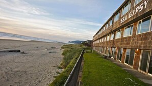 A building named "SEA GYPSY" with a beach view, a grassy area, and a fence along the beachfront. - Retro Oceanfront Suite - Pool and Sauna - Second Floor - Sleeps 4 (Lincoln City)