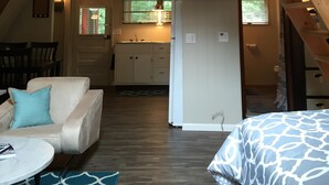 Un espacio tipo loft con balcón de madera, kitchenette, sofá y cama estampada.