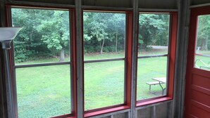 Una habitación con tres ventanas grandes, una puerta roja y vista a un patio cubierto de césped.