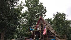 Una casita de juegos de madera con rampa y escaleras, rodeada de árboles.