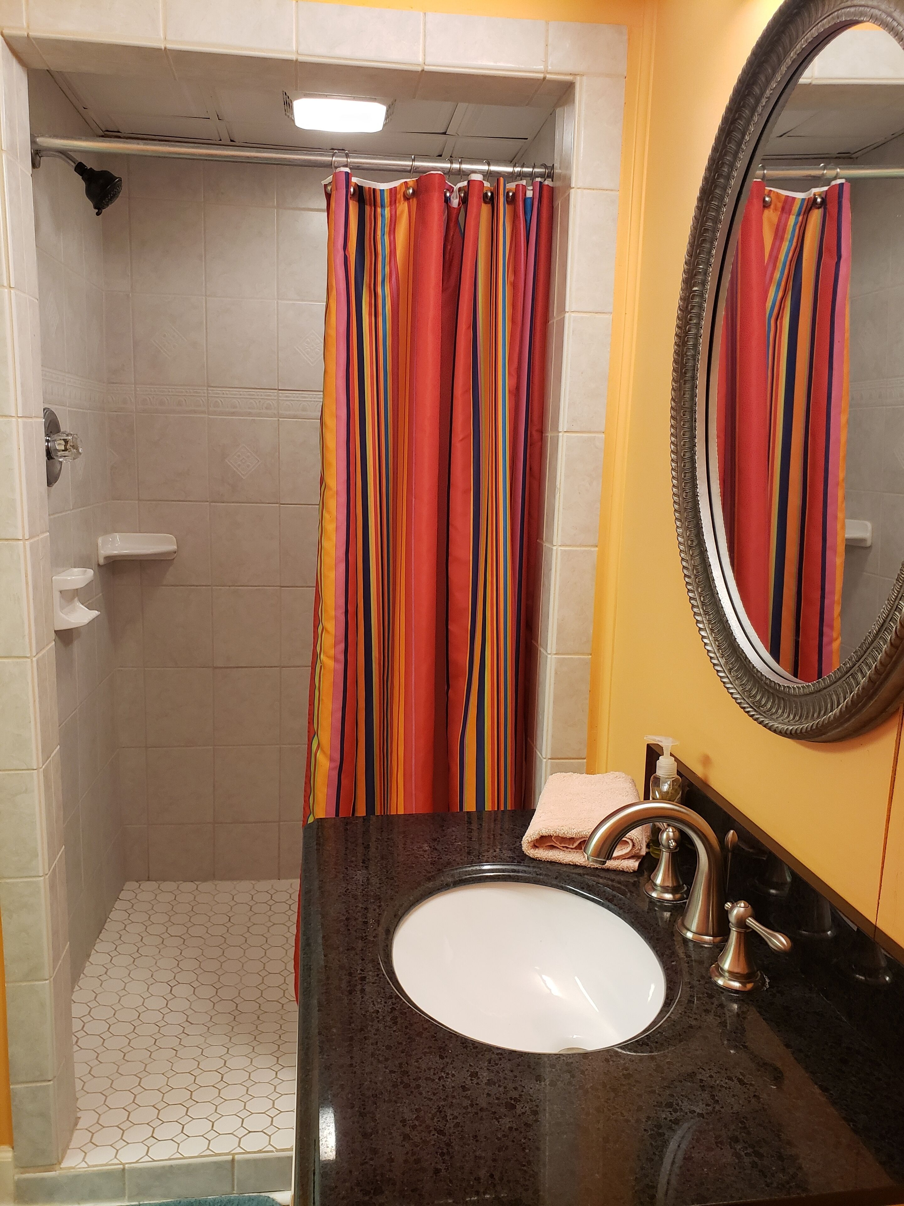 A bathroom with a shower, a sink with a mirror, and a towel.