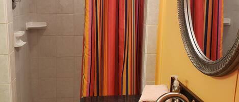 A bathroom with a shower, a sink with a mirror, and a towel.