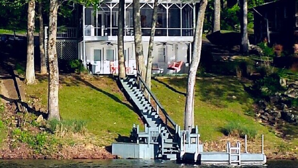Ein Hausboot mit einer Treppe zu einem Deck, umgeben von Bäumen und einem Steg.