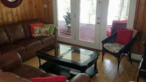 Ein Wohnzimmer mit einem braunen Ledersofa, einem Glastisch und einem Korbstuhl.