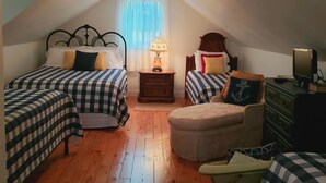 Ein gemütliches Schlafzimmer im Dachgeschoss mit zwei Betten, einem kleinen Tisch, einem Sessel und einer Kommode.
