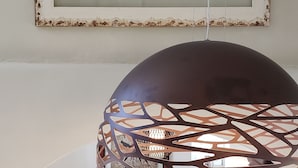 A living room with a grey sofa, a coffee table, a wire chair, and a wooden table. A large framed artwork hangs on the wall above the sofa. - Pleiades Villa, Near Ornos Beach (Mykonos)