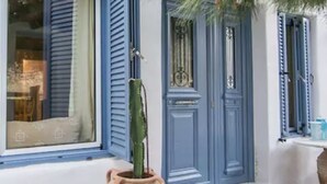 A building with blue shutters and a large potted cactus on the porch. - Pleiades Villa, Near Ornos Beach (Mykonos)