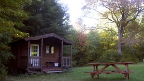 Eine Holzhütte mit Veranda und Picknicktisch in einem bewaldeten Gebiet.