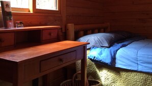 Ein Zimmer einer Holzhütte mit einem Bett, einem Schreibtisch und einem Fenster.
