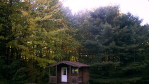 Eine kleine Holzhütte mit Veranda und Picknicktisch inmitten eines bewaldeten Gebietes.