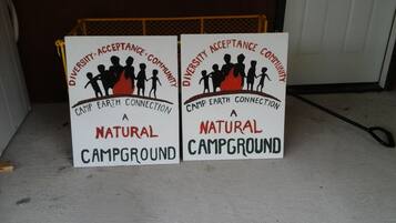 Two signs for a natural campground with diversity and community acceptance messages.