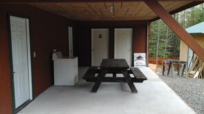 A covered outdoor area with a picnic table, a small white cabinet, and two doors. - Family Friendly Cabin - Sleeps 4, Hiking, Mountain Biking, Beautiful & Private (Freeville)
