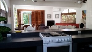 Een keuken met een gasfornuis, een eethoek met stoelen en een bank, en een televisie.