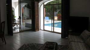Een ruime woonkamer met een grote schuifpui die uitkomt op een terras met een zwembad.