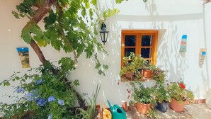 A white building with a window, potted plants, and a tree with blue flowers. - Apartment with a Mountain View and Shared Pool (Montefrio)