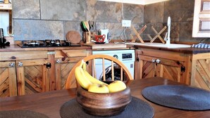 A kitchen with wooden cabinets, a stove, and a dining table with a woven placemat and a wooden bowl with bananas. - Apartment with a Mountain View and Shared Pool (Montefrio)
